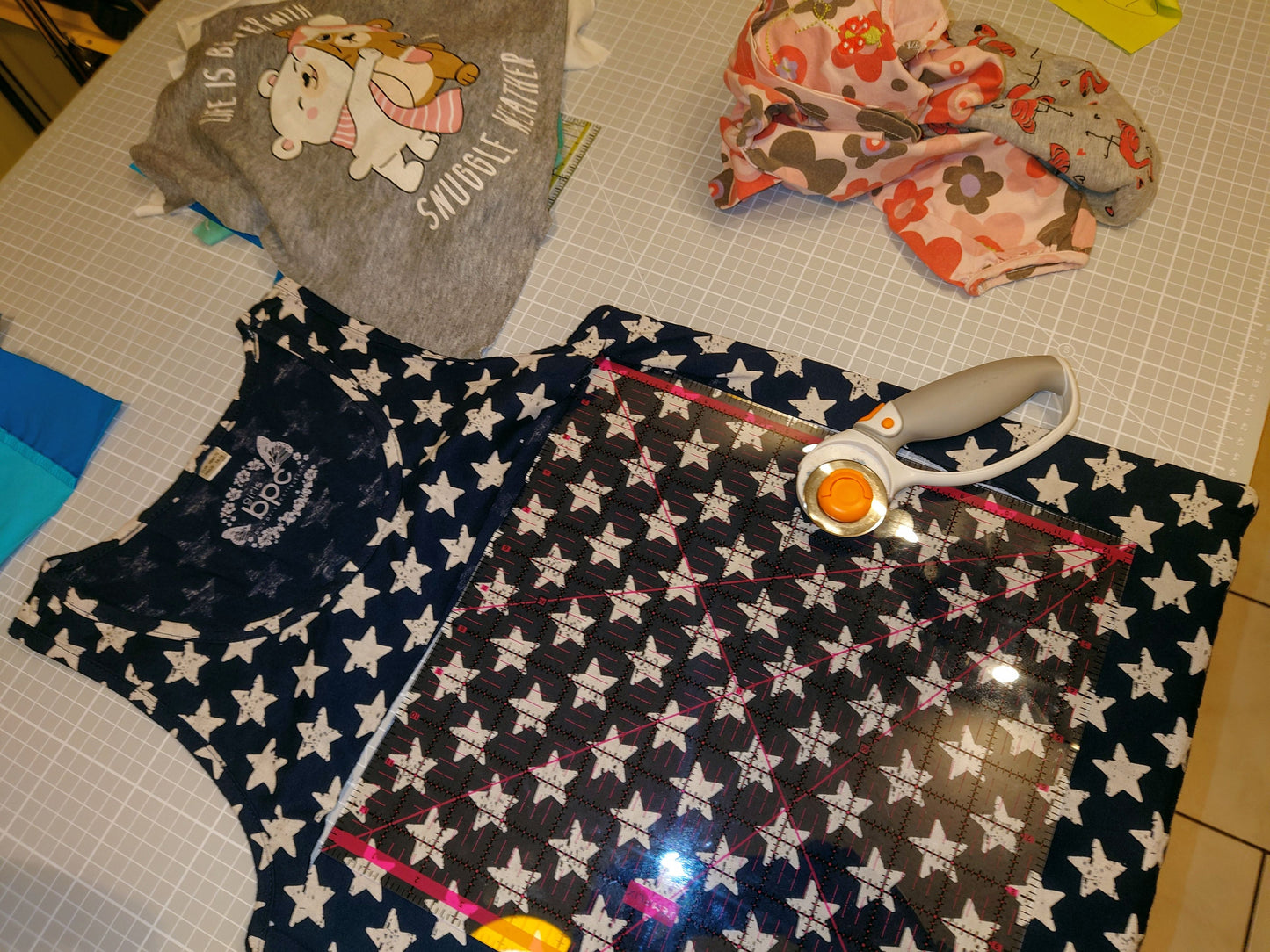 Ein marineblaues Kinderkleid mit weißen Sternen bedruckt. Das Kleid liegt flach auf einer Schneidematte mit einem Rollschneider und einem Lineal. 