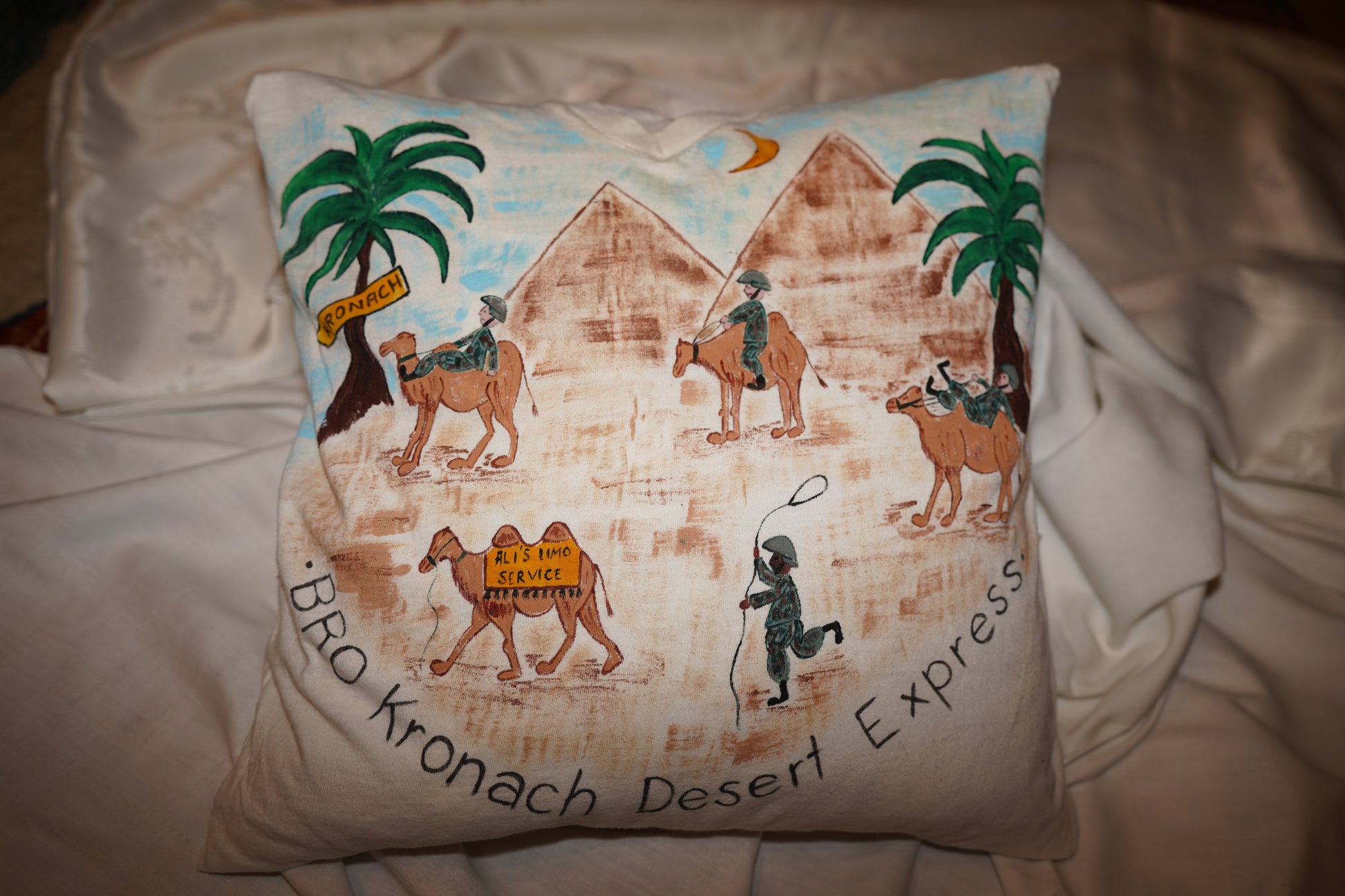 Ein Kissenbezug aus einem T-Shirt von vorne. man sieht den Aufdruck einer Szene in der Wüste mit Kamelen und Pyramiden.