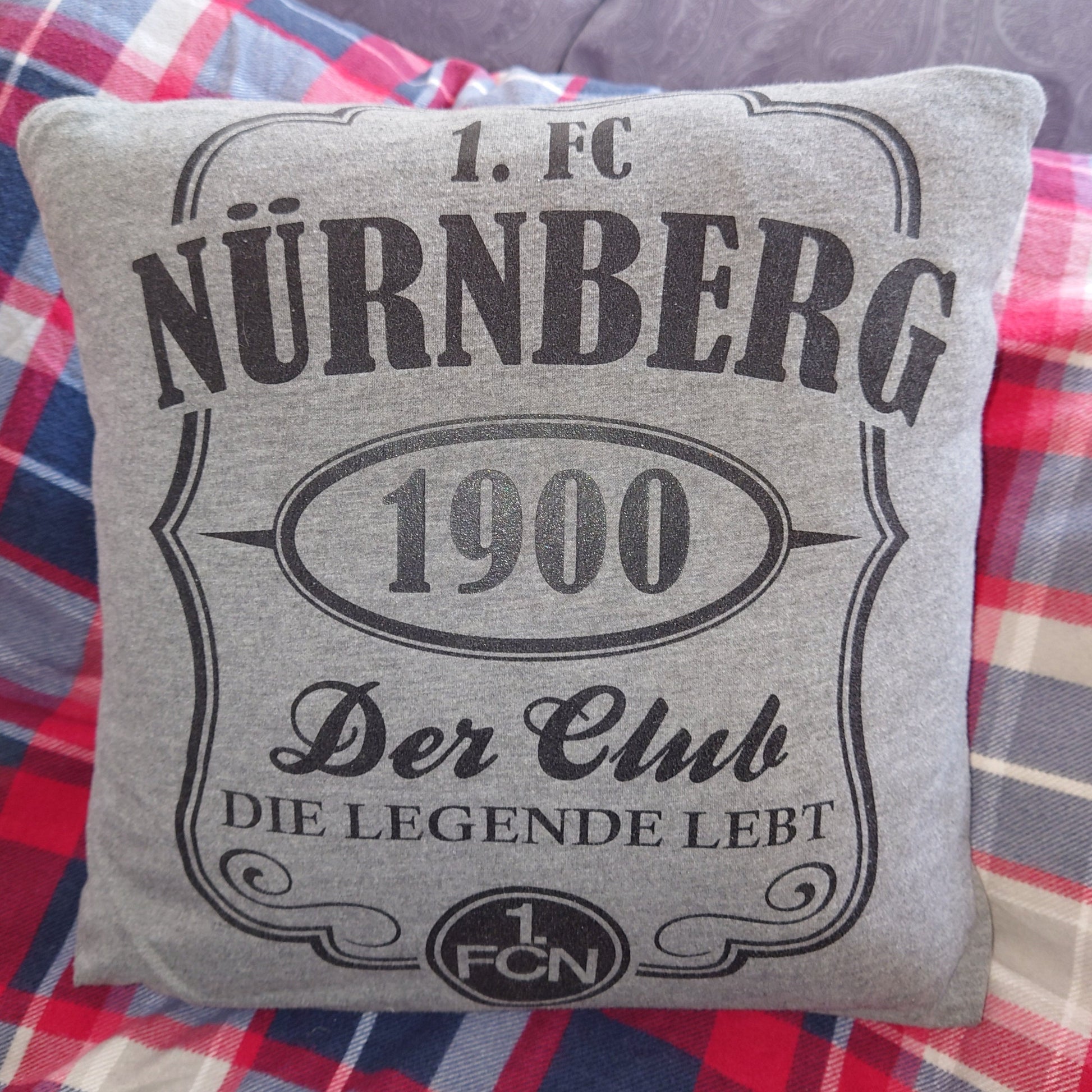 Ein Kissen mit einem Bezug, der aus einem Fußball-Fan-T-Shirt genäht wurde. Man sieht die Vorderseite.